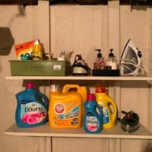 Two Shelves of Clothes Cleaning Items on Shelf in Basement by Washer and Dryer